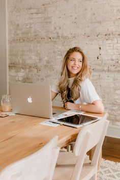 a woman sitting at a table with an apple laptop in front of her, smiling