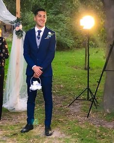 a man in a blue suit standing next to a white and green wedding arch with flowers on it