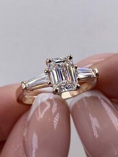 a woman's hand holding an engagement ring with three baguettes on it