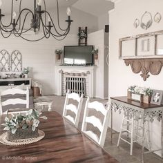 a dining room table with white chairs and a tv on the wall above it, in front of a fireplace