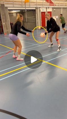 two women are playing with tennis balls in an indoor court while another woman watches from the sidelines