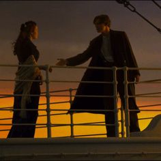 two people standing on the deck of a ship at sunset, one is holding his arm around the other's shoulder