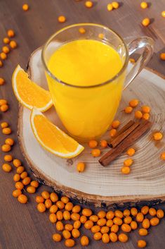 a glass mug filled with orange juice surrounded by cinnamon sticks