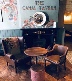 two chairs and a table in front of a fireplace with the canal tavern sign above it