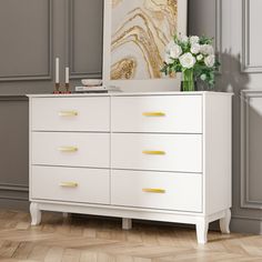 a white dresser with gold handles and flowers on top