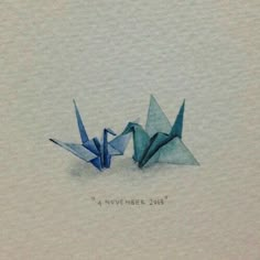 two blue origami birds sitting next to each other on top of a piece of paper