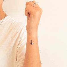 a woman with a small anchor tattoo on her left arm, holding onto the wrist