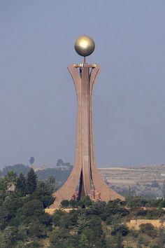 a tall tower with a golden ball on top in the middle of trees and hills