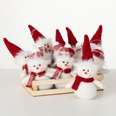 small snowmen in red and white knitted hats sit on a wooden sled