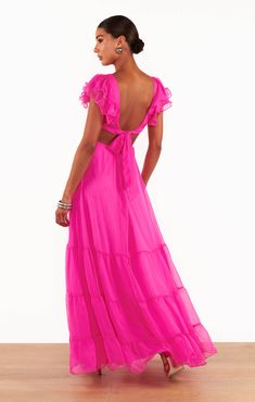 Play up the romance with the Christine Maxi Dress in Shocking Pink Chiffon. With its flowy silhouette and enticing bodice cut-out, this maxi is ideal for showcasing a hint of skin, while the charming rosette detail adds a nice feminine touch. The playful flutter sleeves and tiered ruffled hem add a romantic flair, ensuring you'll be twirling on the dance floor all night long. Complete your look with your favorite heels and dainty jewelry for an elevated look perfect for your next special event. Flirty Bridesmaid Maxi Dress, Flowy Floor-length Pink Dresses, Pink Floor-length Dress With Flowy Skirt, Pink Floor-length Flowy Dress, Pink Tiered Maxi Dress For Evening, Chic Tiered Maxi Dress For Bridesmaids, Pink Tie Back Floor-length Dress, Pink Floor-length Dress With Tie Back, Flirty Chiffon Maxi Dress