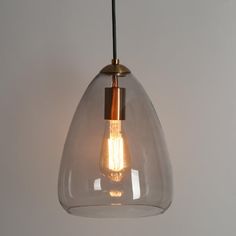 a clear glass pendant light hanging from a ceiling fixture with a gold metal fitting on the end