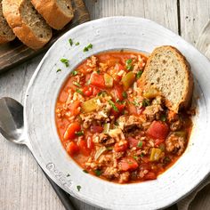 a white bowl filled with soup next to bread on top of a cutting board and spoon