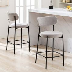 two gray stools sitting in front of a white counter top next to a window