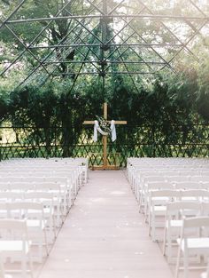 an outdoor wedding setup with white chairs and a cross at the end of the aisle