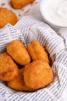 some fried food is in a basket and on the table next to a bowl of ranch dressing