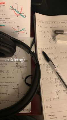 a pair of black headphones sitting on top of paper with calculations and pen next to it