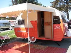 an orange and white camper parked in a parking lot next to other vehicles with awnings