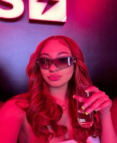 a woman with red hair and sunglasses is holding a glass in front of her face