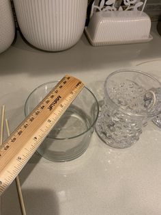 a wooden ruler sitting on top of a counter next to some glass bowls and glasses