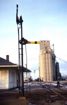 a railroad crossing signal in front of a grain silo and building on the other side