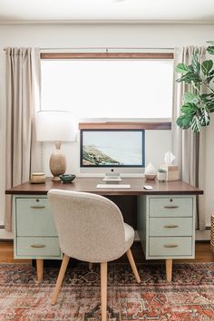 a desk with a computer on top of it in front of a window and a potted plant