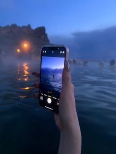 someone holding up their cell phone to take a photo in the water at night time