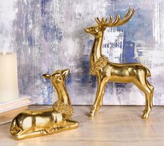 two golden deer figurines sitting next to each other on a wooden floor in front of a blue and white wall