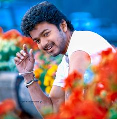 a man standing in front of flowers making the peace sign with his hand and smiling