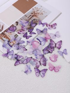 purple and pink butterflies are scattered on the floor next to a white book with photos in it