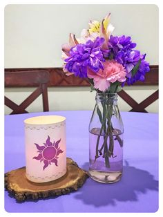 purple flowers in a vase next to a lit candle on a wooden slice at the end of a table