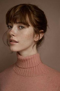 a woman with freckled hair wearing a pink turtle neck sweater and looking off to the side