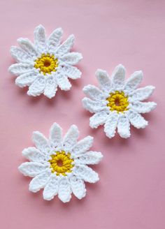 three crocheted white and yellow flowers on a pink surface with one flower in the center