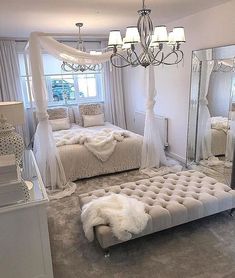 a bedroom with white bedding and chandelier hanging from the ceiling in front of a large mirror