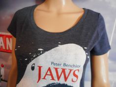 Peter Benchley, Jaws t-shirt. Jaws, the famous novel turned adapted to a screenplay resulting in one of the most famous movies ever made. Fitted tee; curved, fitted for a female's body/ A blue tee featuring graphic and author's name on front. Bright. Fun. Perfect slight fade. Bold yet dainty. Clean. No issues. Ready to wear. Tagless tag states Medium and the measurements are: 23 1/2 inches long (top to bottom), 17 inches across (armpit seam to armpit seam). https://vintagethisexit.etsy.com Jaws is a 1974 novel by American writer Peter Benchley. It tells the story of a great white shark that preys upon a small resort town and the voyage of three men trying to kill it. The novel grew out of Benchley's interest in shark attacks after he learned about the exploits of Montauk, New York shark fi Fitted T-shirt With Front Print And Crew Neck, Fitted Crew Neck T-shirt With Front Print, Fitted Crew Neck Shirt With Screen Print, Fitted Graphic Tee For Fan Merchandise, Fitted T-shirt With Front Print For Fans, Casual Fitted Top For Fan Merchandise, Fitted Crew Neck Shirt With Band Merch, Fitted Short Sleeve T-shirt For Fan Merchandise, Fitted Short Sleeve Top For Fan Merchandise