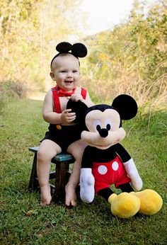 a baby sitting on a bench next to a mickey mouse stuffed animal