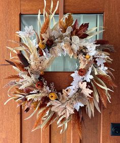 a wreath made out of dried leaves and flowers on a wooden door frame with a glass window behind it