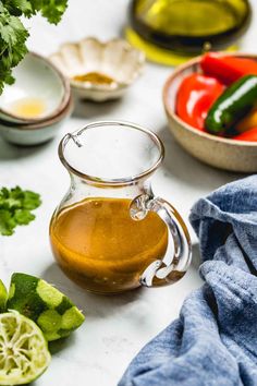 a glass pitcher filled with green liquid next to bowls of fresh vegetables and sauces