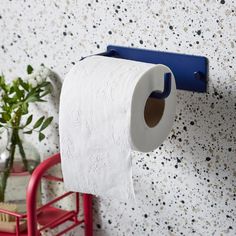 a roll of toilet paper hanging on a wall next to a red chair and potted plant