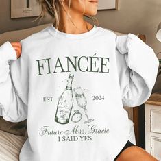 a woman sitting on a bed wearing a white sweatshirt with the words france and two champagne glasses printed on it