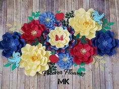 paper flowers are arranged on a wooden surface with green leaves and red, yellow, blue, and white flowers