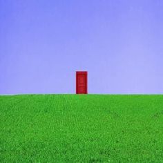 an open red door stands in the middle of a green field with a blue sky behind it