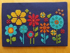 a cross - stitched card case with flowers and birds on it, sitting on a wooden table