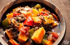 a wooden bowl filled with meat and vegetables on top of a cloth covered tablecloth