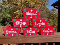 six red and green christmas baskets sitting on top of a wooden bench in front of trees