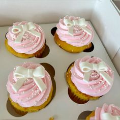 cupcakes with pink frosting and white bows in a box