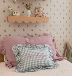 a bed with pink and blue pillows on top of it next to a shelf filled with figurines