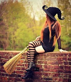 a woman sitting on top of a brick wall wearing a witch costume and holding a broom