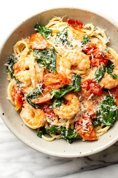 pasta with shrimp, spinach and tomato sauce in a white bowl on a marble surface