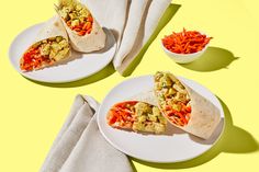 two burritos on plates with carrots and other food items next to them