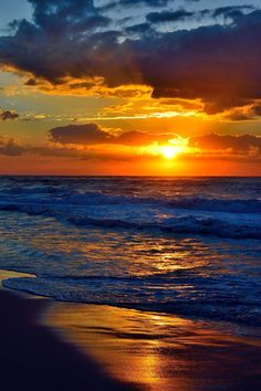 the sun is setting over the ocean with clouds in the sky and waves on the beach